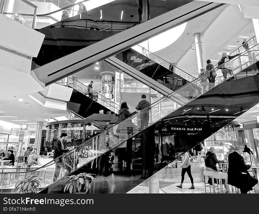 People riding escalator inside modern shopping center in black and white. People riding escalator inside modern shopping center in black and white.