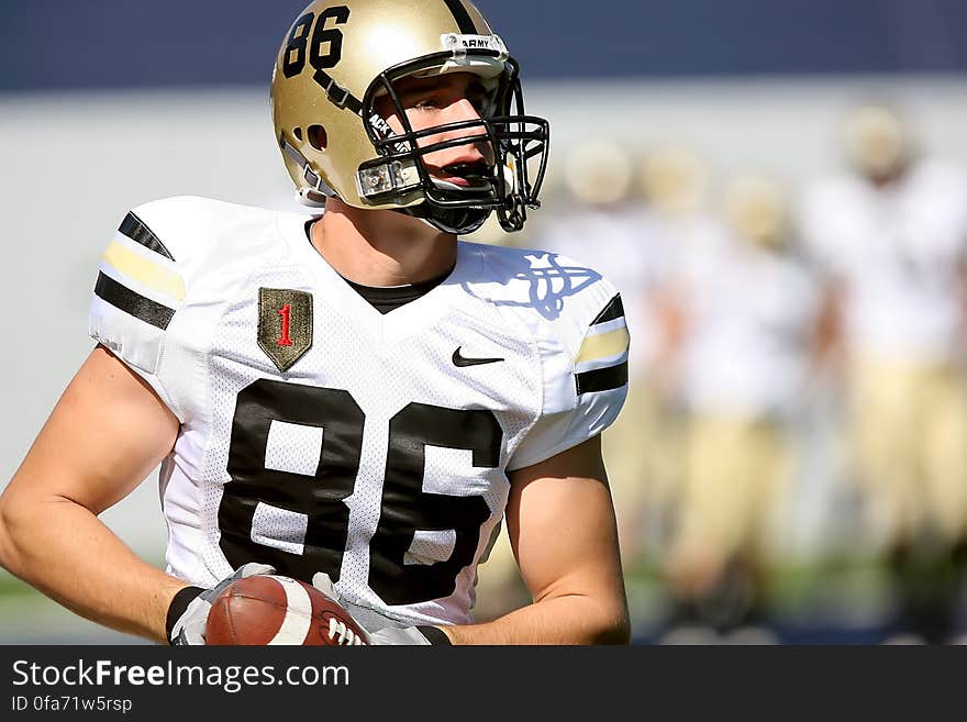 Portrait of football player in uniform and helmet holding ball during game. Portrait of football player in uniform and helmet holding ball during game.