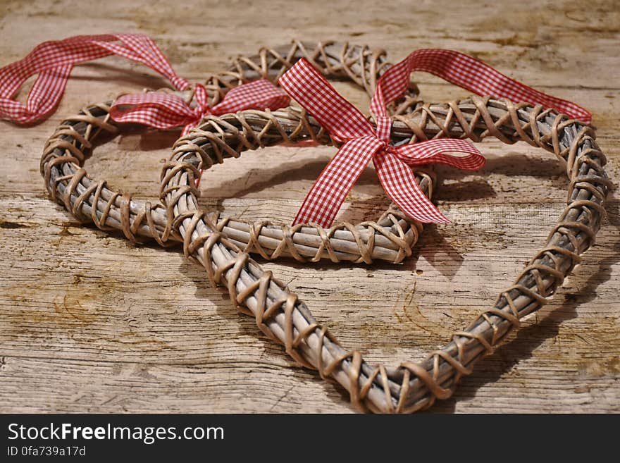 Close up of rustic wicker hearts with checkered ribbon bows on wooden table. Close up of rustic wicker hearts with checkered ribbon bows on wooden table.