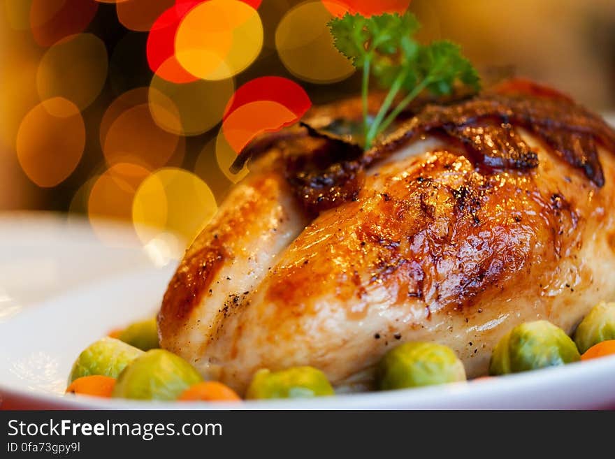 Close up of roasted chicken on white china plate with brussels sprouts and carrots with bokeh light background. Close up of roasted chicken on white china plate with brussels sprouts and carrots with bokeh light background.