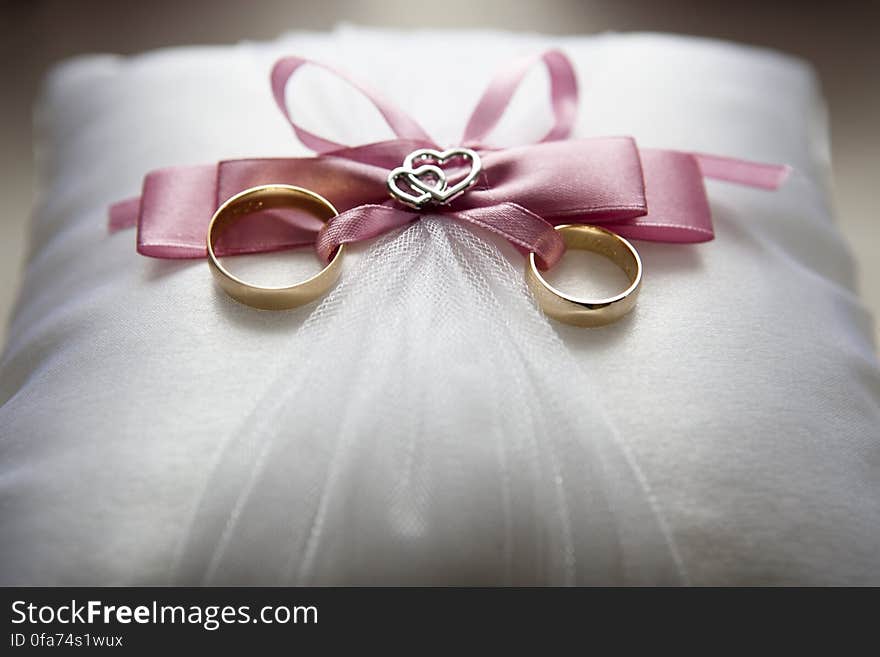 Close up of gold wedding rings on satin pillow with pink bows. Close up of gold wedding rings on satin pillow with pink bows.