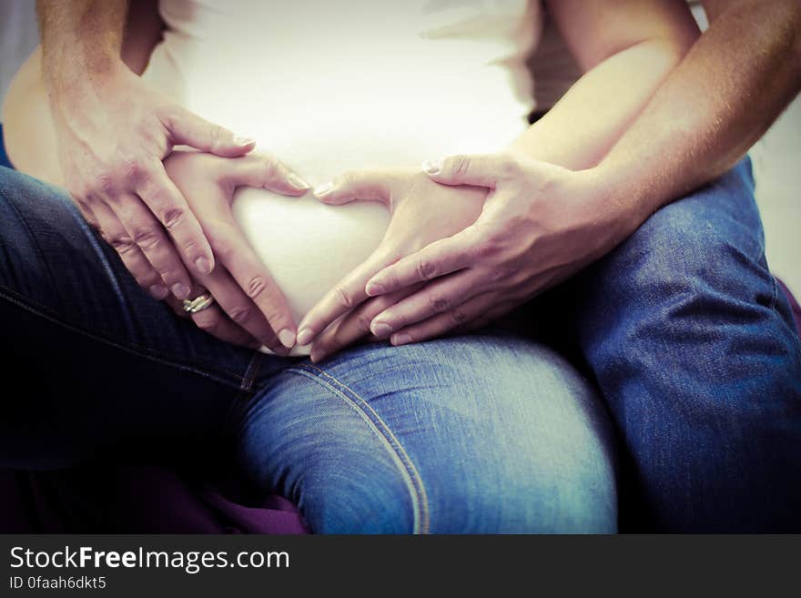 Pregnant woman and partner with hands forming love heart over stomach.