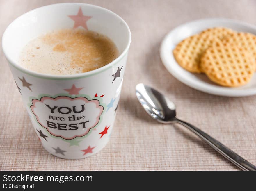 Cup of coffee on table with biscuits and spoon, message reads you are the best.