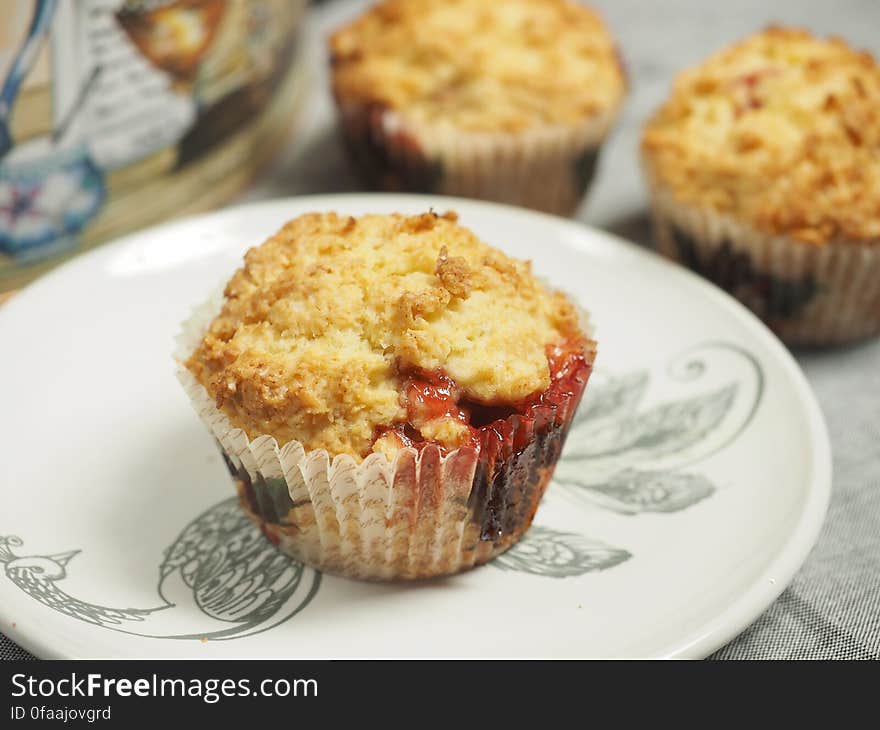 Closeup of freshly baked cherry muffins with one on plate in case.