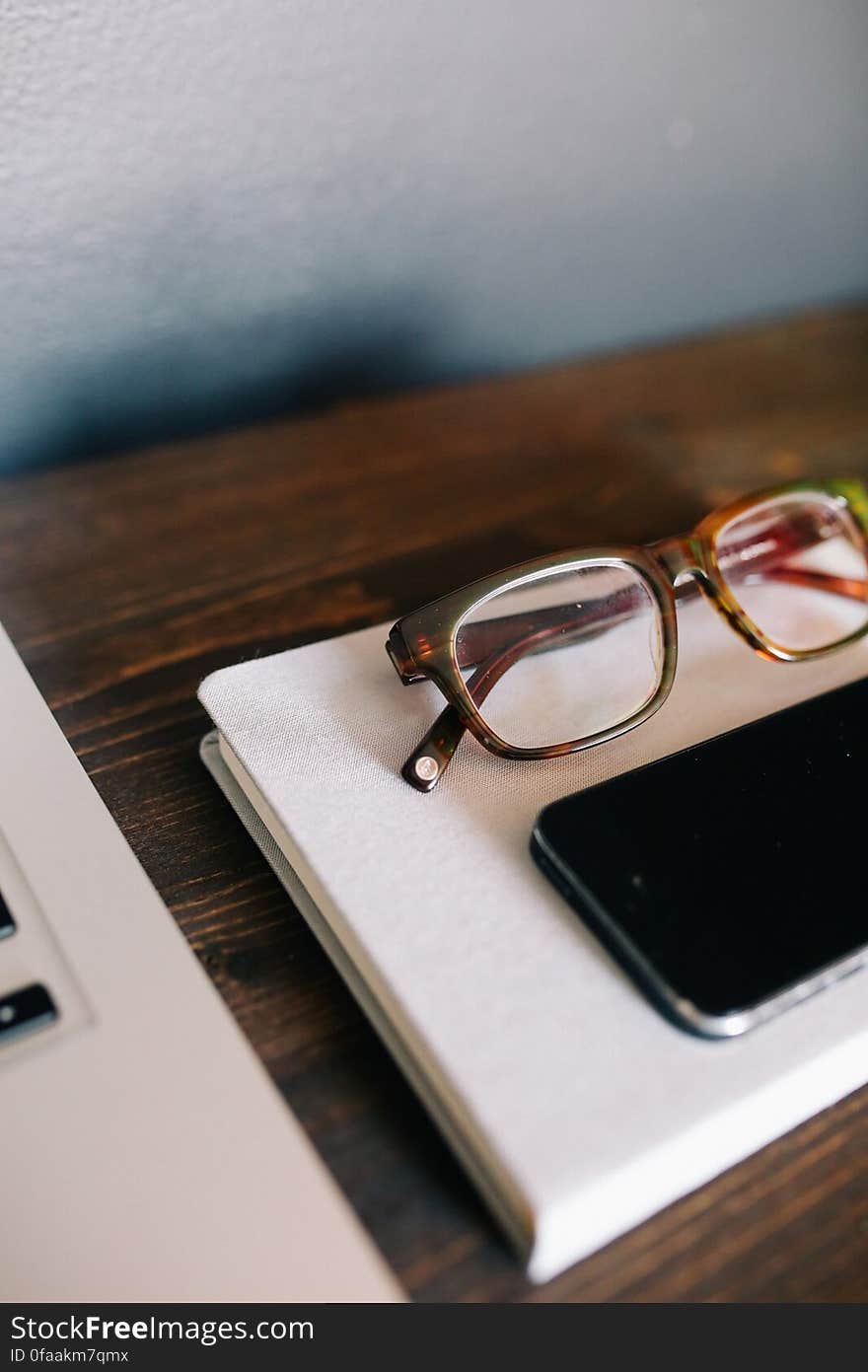 A close up of smartphone and eyeglasses on a notebook on a desk. A close up of smartphone and eyeglasses on a notebook on a desk.