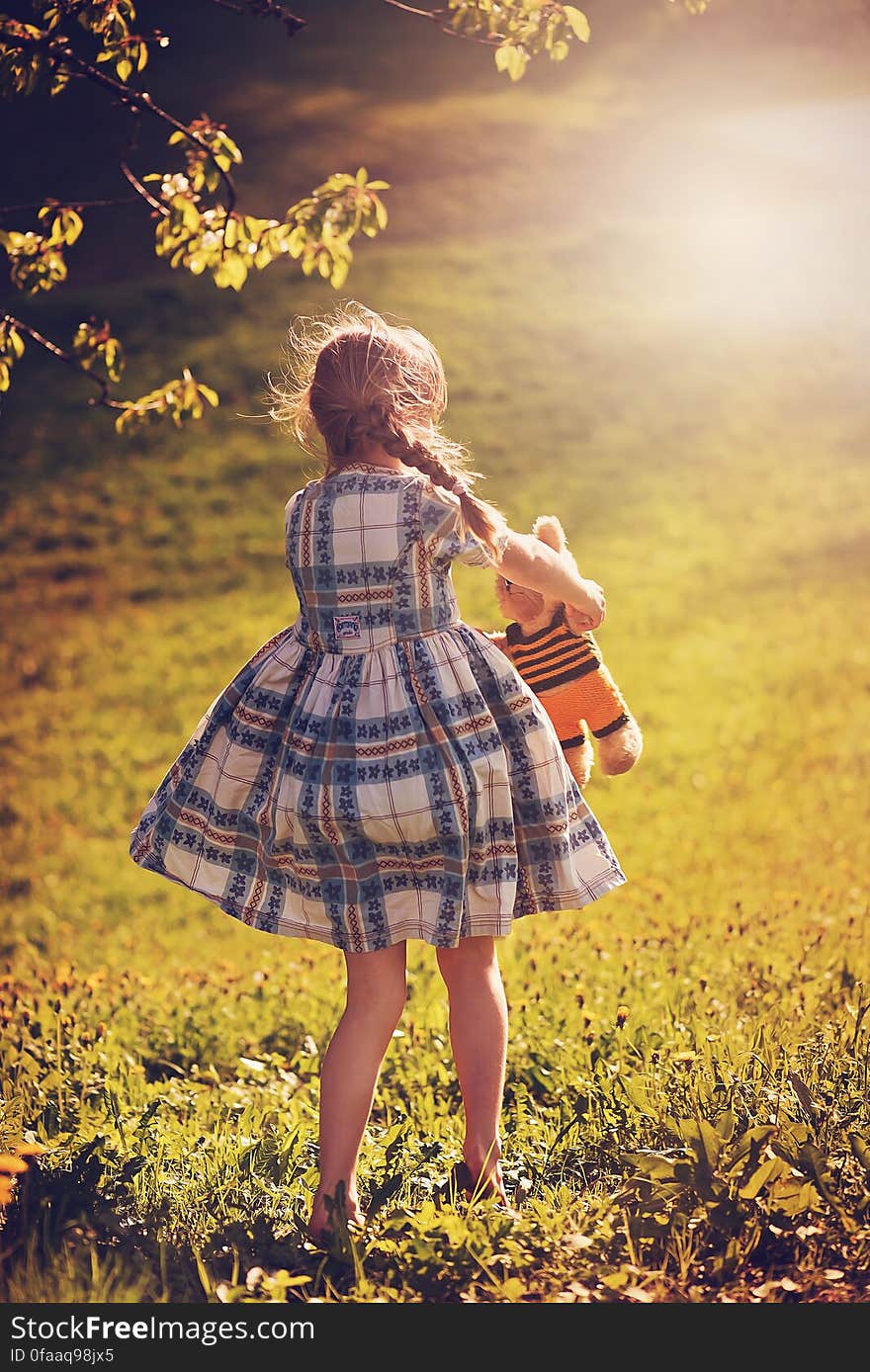 A girl in dress with a teddy bear walking out in the sun. A girl in dress with a teddy bear walking out in the sun.