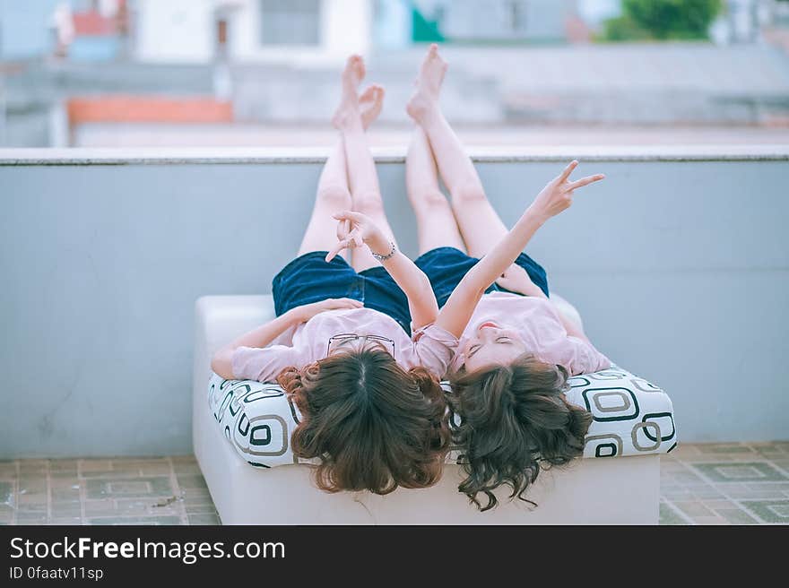 A pair of girls in identical clothing lying down and making peace sign. A pair of girls in identical clothing lying down and making peace sign.