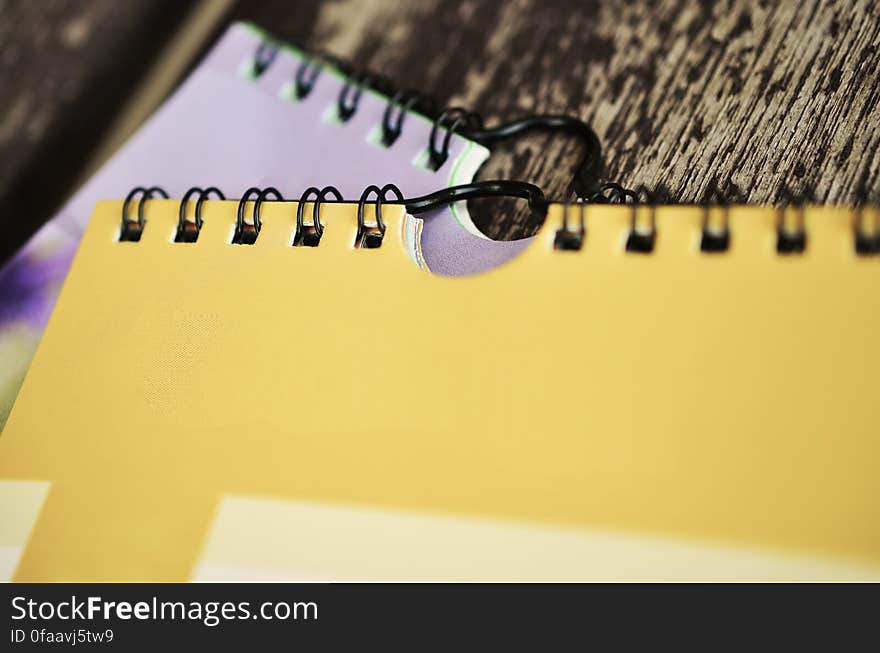 Two spiral bound notebooks with selective focus on the yellow one and the mostly white one a blur in the background.