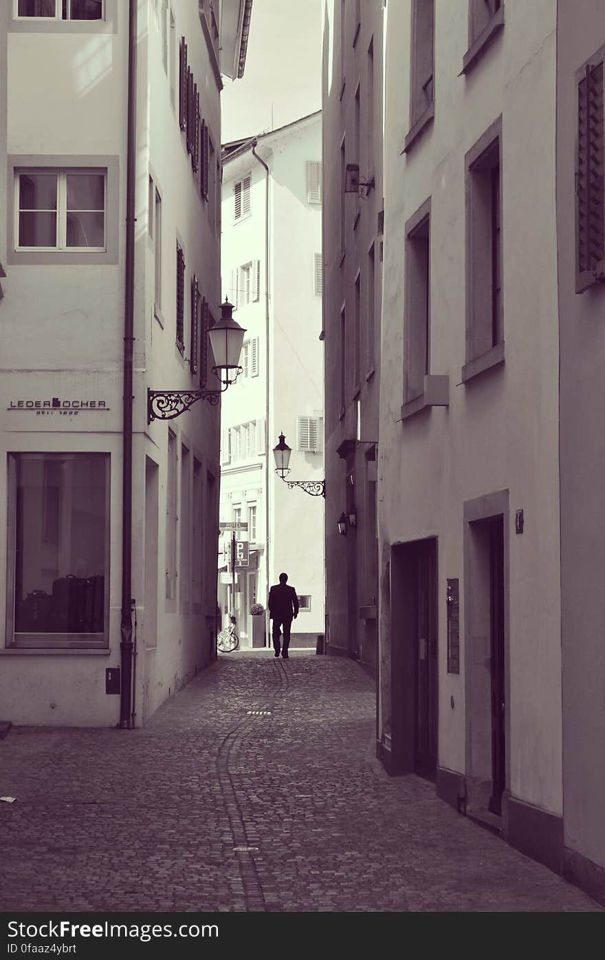 A monochrome photo of a man walking along a cobbled alley in an old town. A monochrome photo of a man walking along a cobbled alley in an old town.