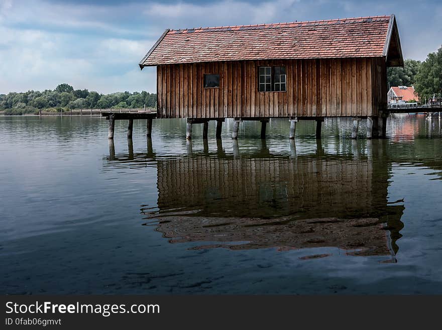 Wooden boathouse on stilts reflecting in waters on sunny day. Wooden boathouse on stilts reflecting in waters on sunny day.