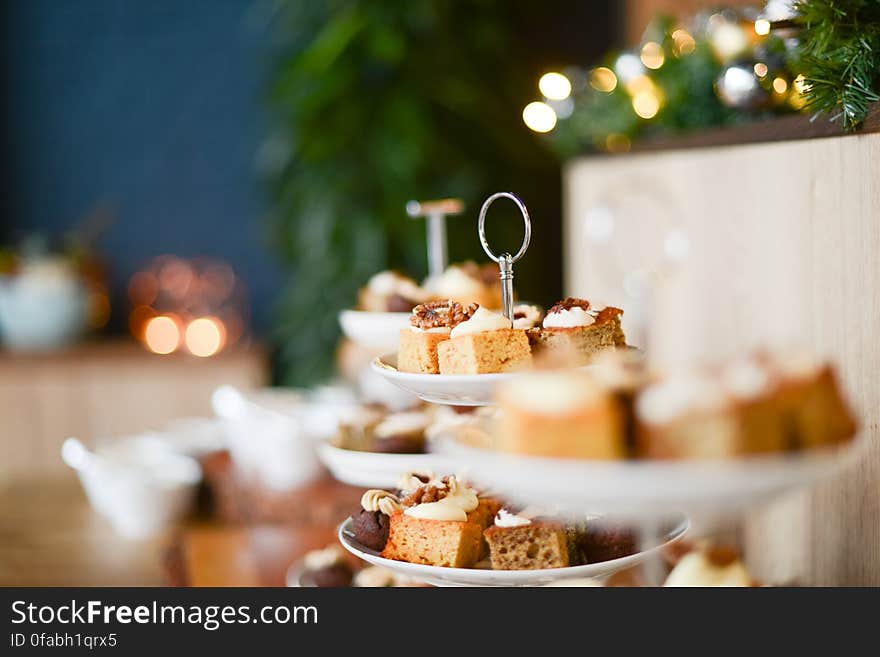 Pieces of iced cakes laid out on plates with selective focus two particular slices and a Christmas tree in the blurred background. Pieces of iced cakes laid out on plates with selective focus two particular slices and a Christmas tree in the blurred background.