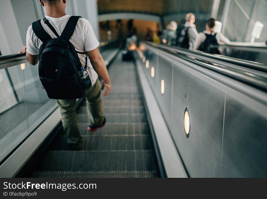 Person Wearing Black Backpack Riding Down the Escalator