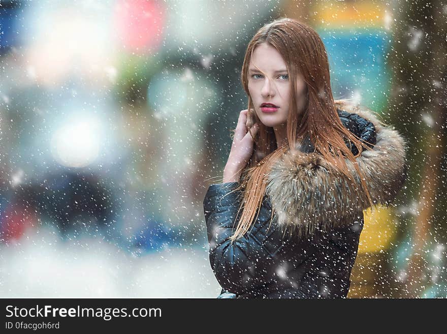 Attractive young woman in a Winter coat with large fur collar posing while snow is falling. Attractive young woman in a Winter coat with large fur collar posing while snow is falling.