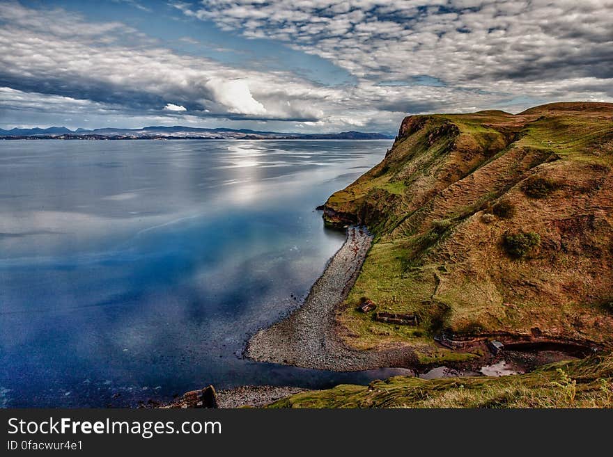 Cliff over waterfront against blue skies with clouds on sunny day.