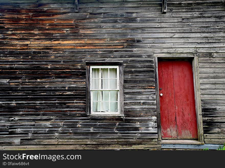 An old wooden cabin with red entrance door.