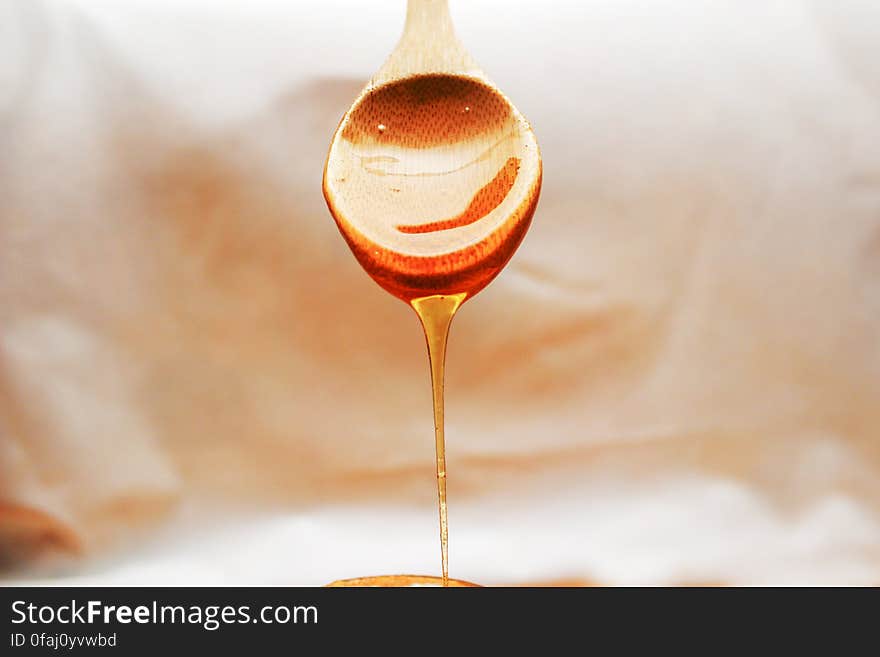 Closeup of teaspoon with honey draining from it (into a honey and lemon drink perhaps) showing slow smooth flow of the viscous liquid, blurred background. .