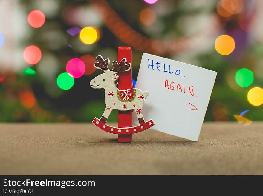 Reindeer Christmas ornament with small sign saying hello again against colorful bokeh lights. Reindeer Christmas ornament with small sign saying hello again against colorful bokeh lights.