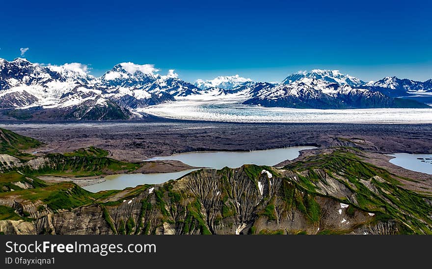 Glacial mountain landscape with melting pools on sunny day with blue skies.