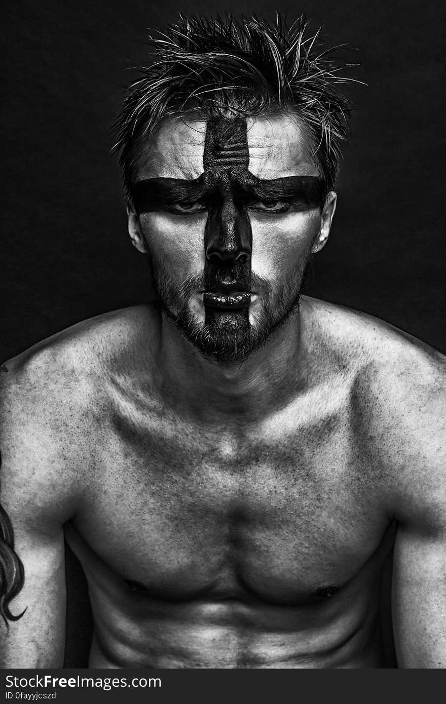 Portrait of man without shirt wearing cross in paint on face in black and white. Portrait of man without shirt wearing cross in paint on face in black and white.