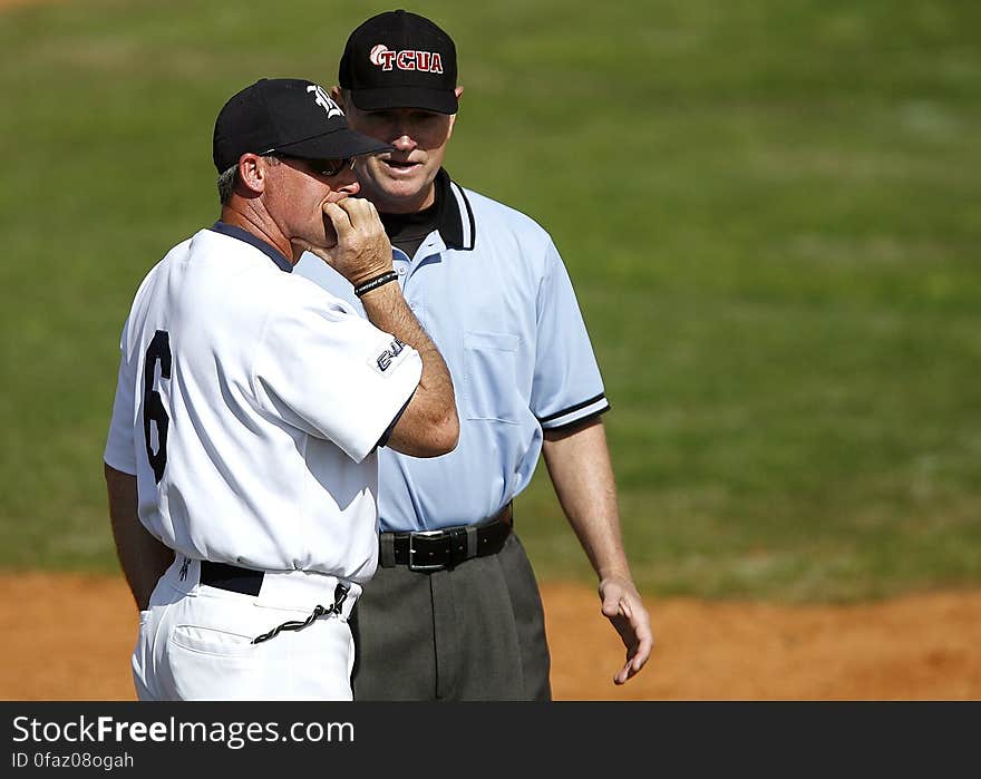 Baseball player talking to umpire or coach on field during game on sunny day. Baseball player talking to umpire or coach on field during game on sunny day.