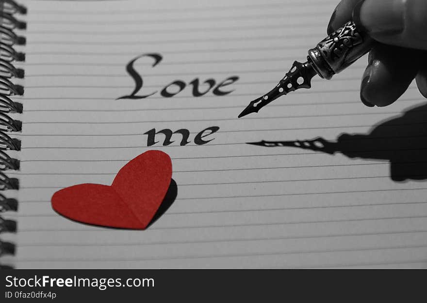 Love me text on lined white page with red heart cut out and fountain pen in hand. Love me text on lined white page with red heart cut out and fountain pen in hand.