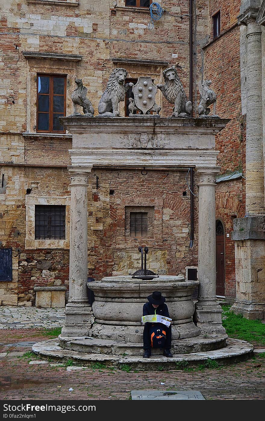 A traveler sitting and reading a map at an old well. A traveler sitting and reading a map at an old well.