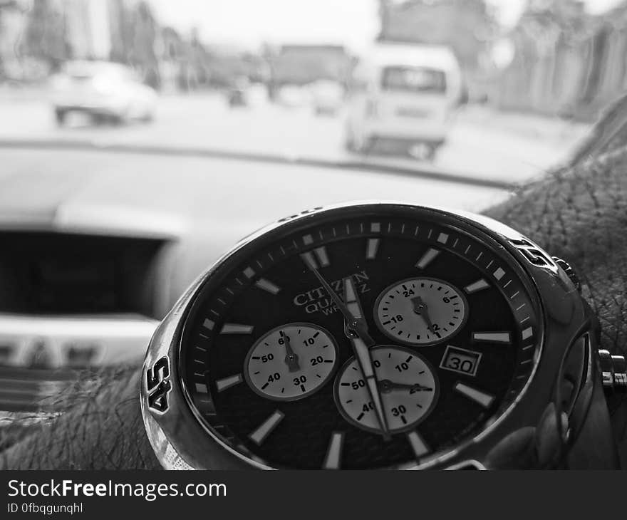 Close up of Citizen quartz watch with precise timing facility on the arm of a driver of a car, with background through windscreen of blurred image of the road and traffic. Close up of Citizen quartz watch with precise timing facility on the arm of a driver of a car, with background through windscreen of blurred image of the road and traffic.