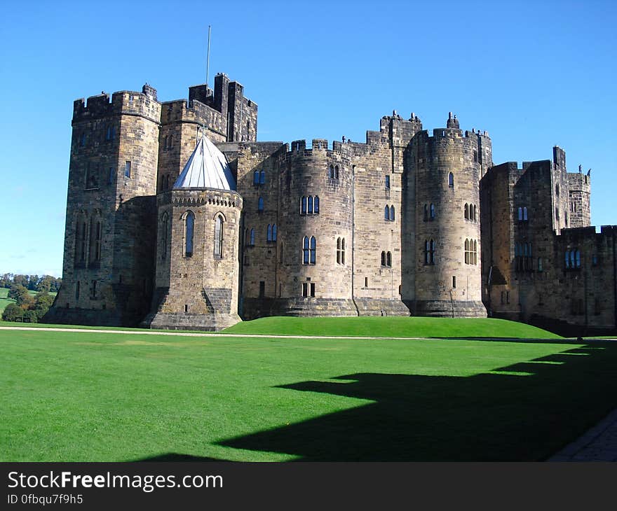 Exterior of Alnwick Castle in Northumberland, England on green lawn on sunny day with blue skies. Exterior of Alnwick Castle in Northumberland, England on green lawn on sunny day with blue skies.