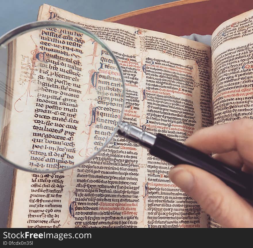 Hand holding magnifying glass over page of antique book. Hand holding magnifying glass over page of antique book.