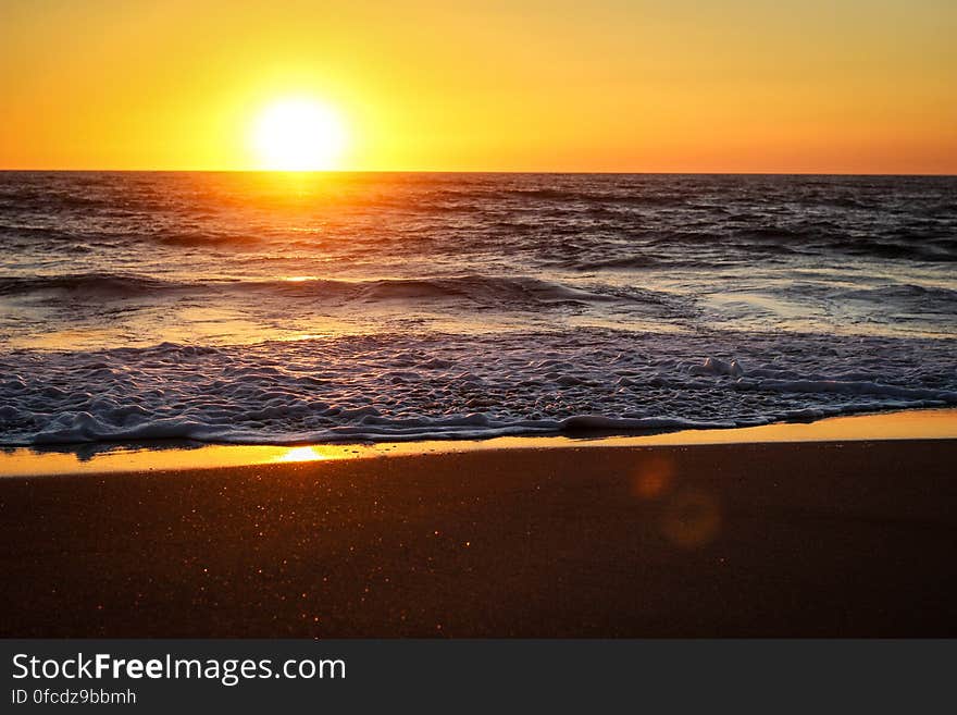 Sunset over horizon along sandy beach with washing waves. Sunset over horizon along sandy beach with washing waves.