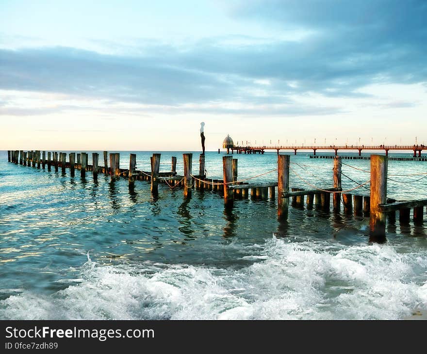 Pylons from old wooden pier in waves off coast on sunny day.