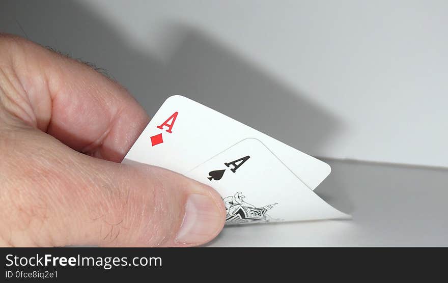 Close up of hand holding pair of aces on desk.