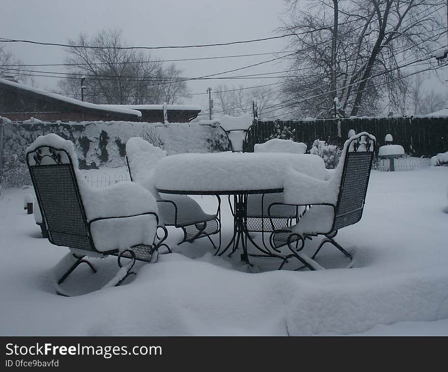 Snow covered patio table and chairs in back yard on overcast day. Snow covered patio table and chairs in back yard on overcast day.
