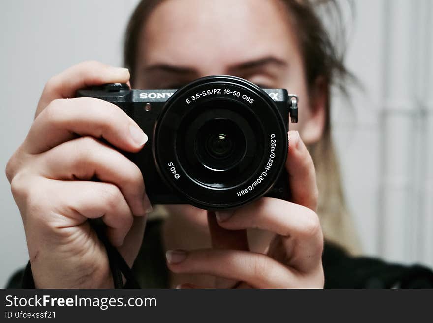 Woman Holding Black Sony Dslr Camera Taking a Photo of Herself at Mirror