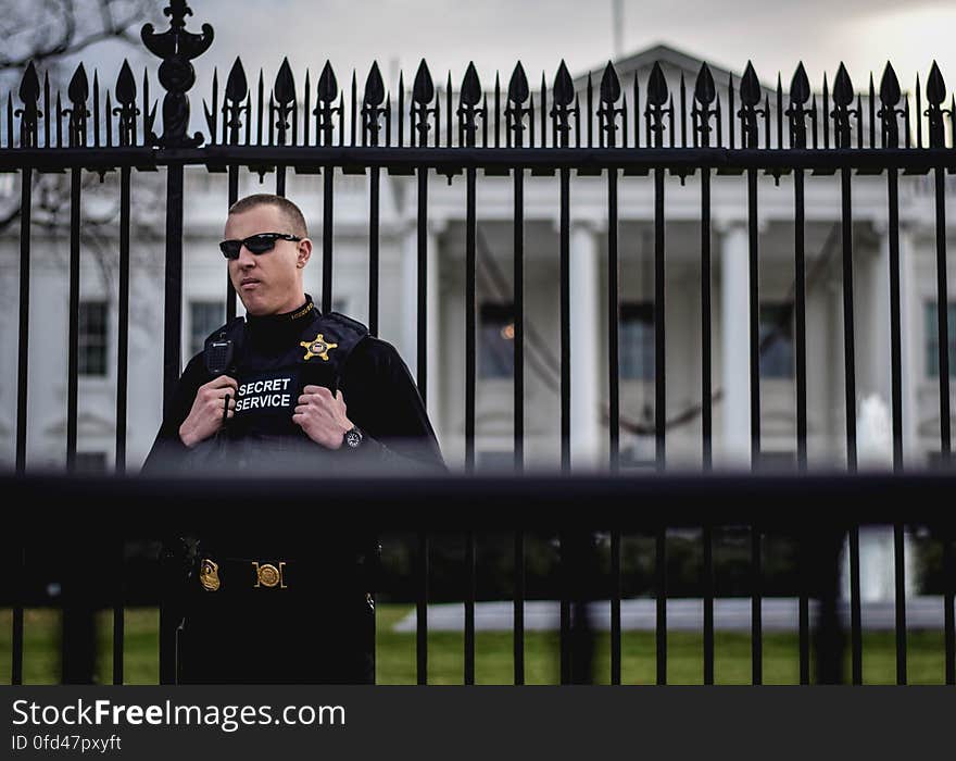 A United States Secret Service agent stands guard between the upgraded security fence and metal barricade &#x28;foreground&#x29; that block off the north lawn of the White House from tourists on Pennsylvania Avenue NW on December 13, 2015. Released into the public domain under a CC0 license. A United States Secret Service agent stands guard between the upgraded security fence and metal barricade &#x28;foreground&#x29; that block off the north lawn of the White House from tourists on Pennsylvania Avenue NW on December 13, 2015. Released into the public domain under a CC0 license.