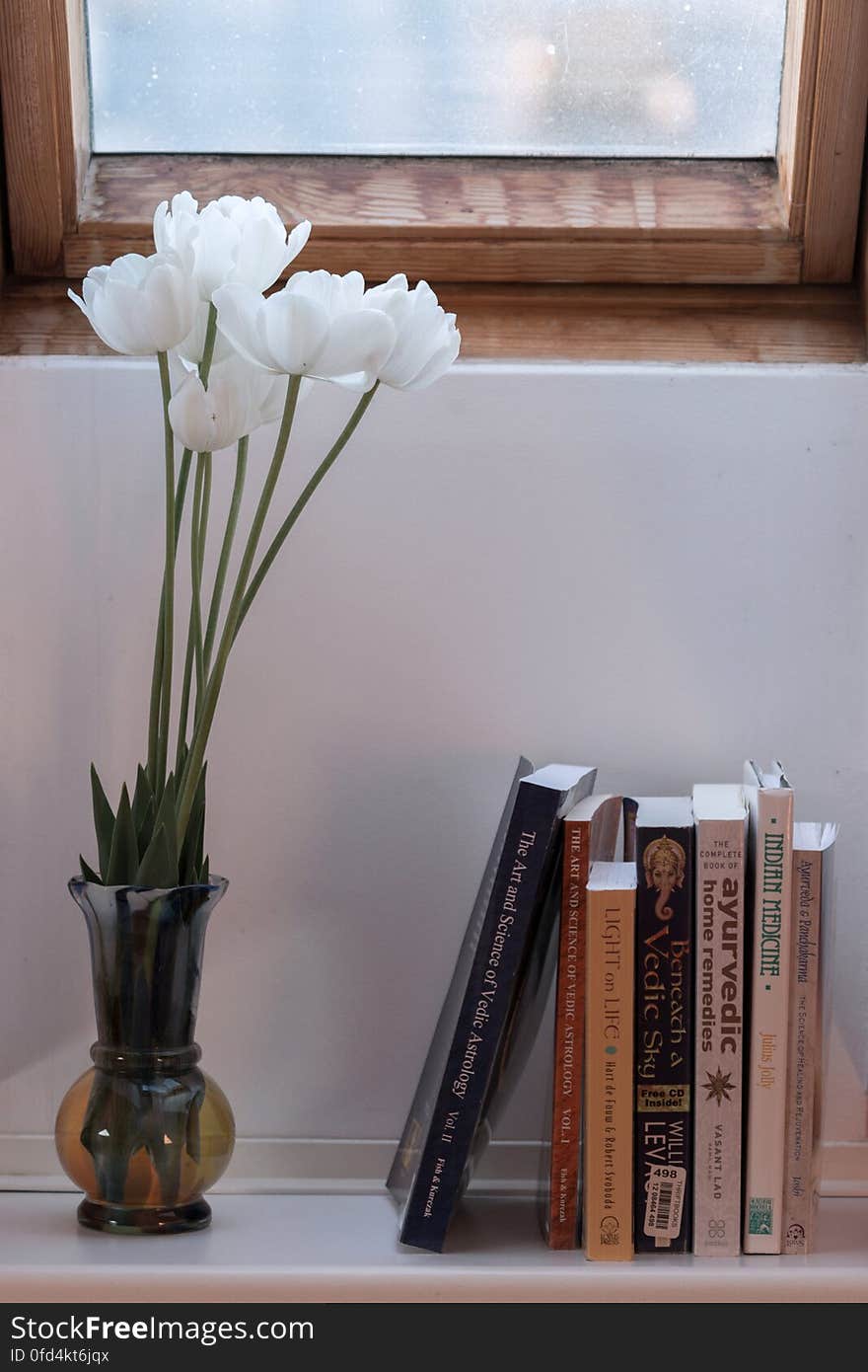 White tulips in a vase on a windowsill, which also has books on ayurveda and astrology standing on it. White tulips in a vase on a windowsill, which also has books on ayurveda and astrology standing on it.