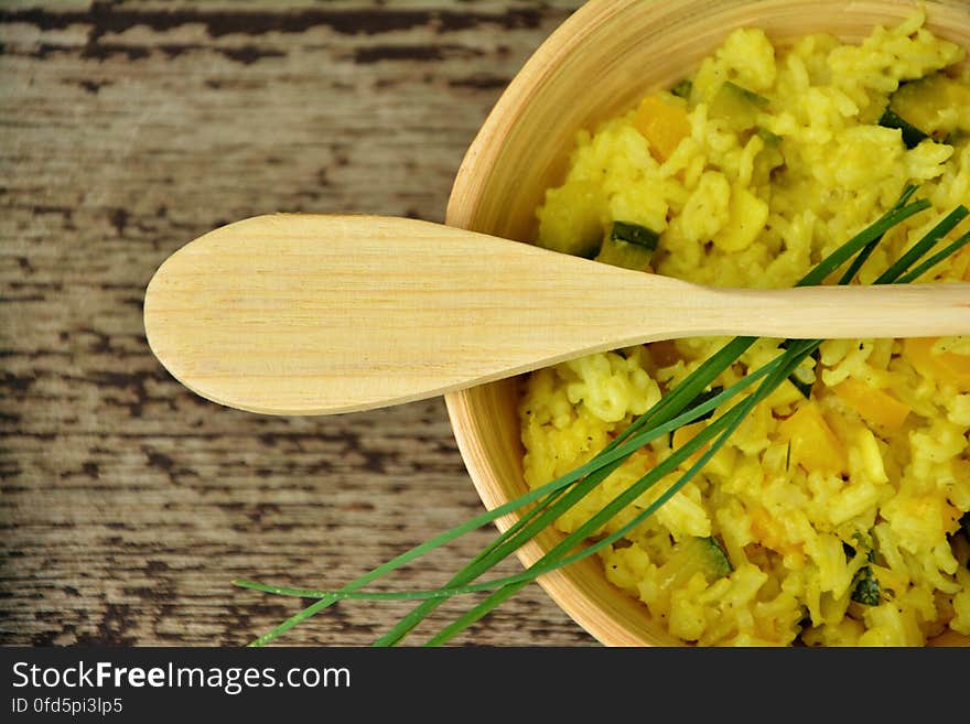 A wooden bowl with rice and vegetables and wooden spoon on top.