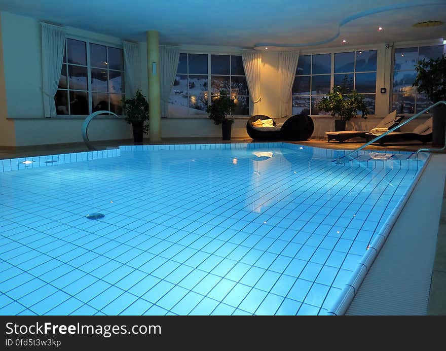 Empty indoor swimming pool with lounge chairs illuminated at night.