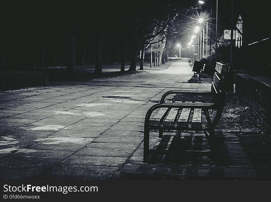 Empty park bench on city sidewalk illuminated at night in black and white. Empty park bench on city sidewalk illuminated at night in black and white.