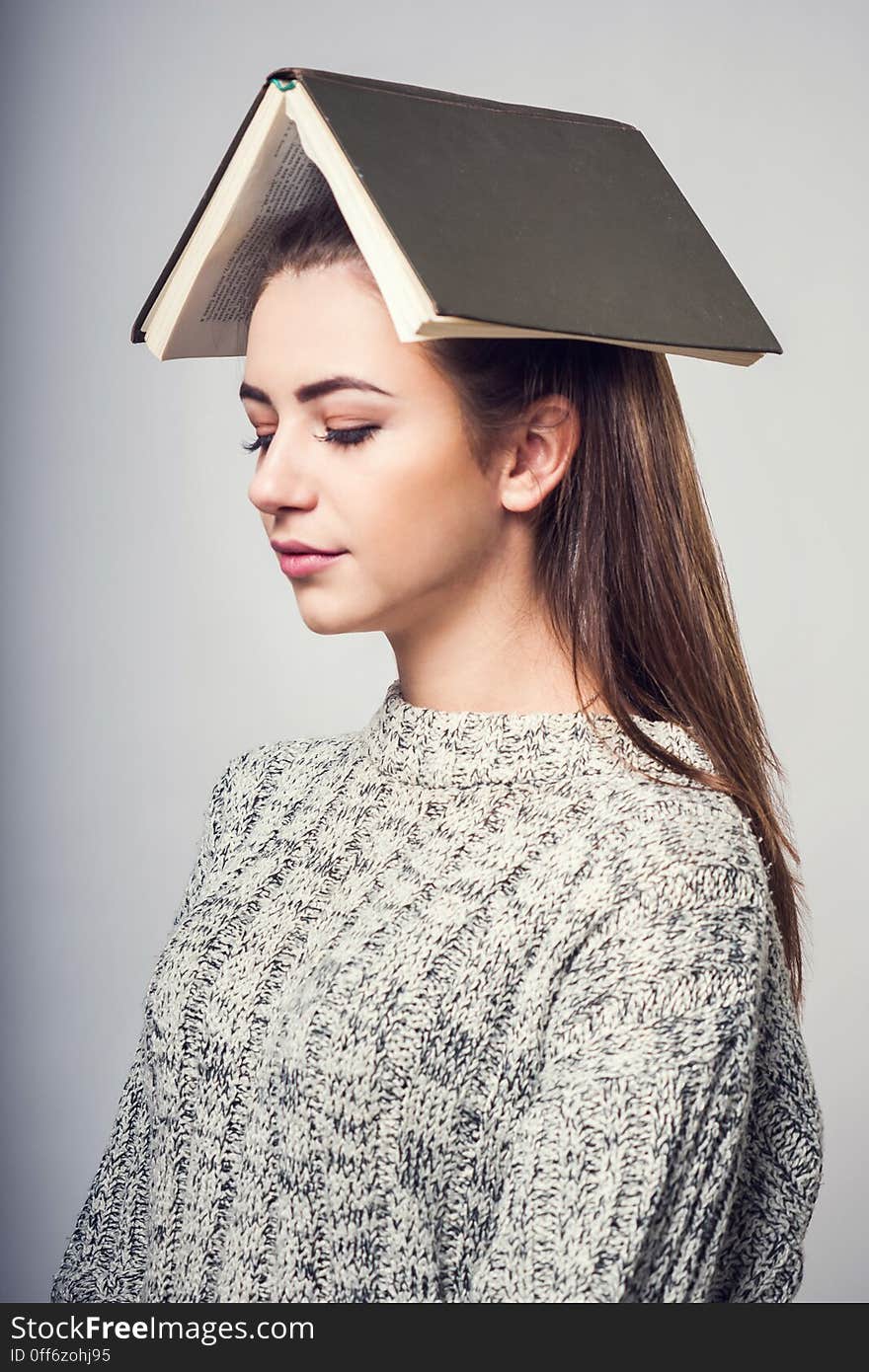 Girl student brunette in a warm sweater, reading a book and dreaming