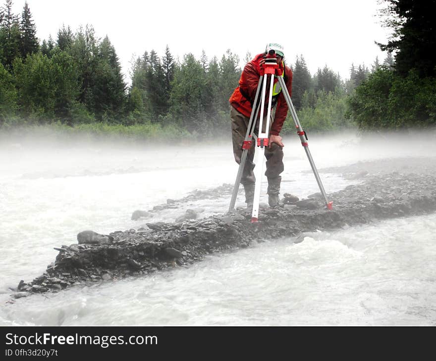 Using Science to Improve Infrastructure — In this photo, we see Paul Schauer &#x28;USGS&#x29; running a level survey for the streambed scour project in Seward, Alaska. The goal of this type of work is to evaluate the scour susceptibility of bridges in order to identify structures that require mitigation of the scour problem, annual monitoring, or near real-time scour monitoring. Bridge scour is​ basically​ the removal of sediment &#x28;like rock, sand, etc&#x29; from around the bridge causing it to weaken. Streambed scour at bridges is the leading cause of bridge failure in the United States. The costs associated with restoring damaged structures are substantial, but the indirect costs associated with the disruption of traffic can be up to five times greater. These costs and the societal repercussions are even greater in Alaska, where alternate land routes between many cities do not exist. Flood damage to two bridges on the George Parks Highway between Anchorage and Fairbanks closed the highway for four days in August 2006 and repair costs to these structures and others damaged during the flooding are estimated at over 13 million dollars. Learn more about this project at bit.ly/AKScour.