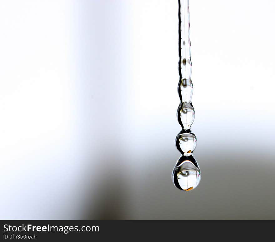 Some water drops hanging from the kitchen faucet, reflecting some parts of the kitchen.