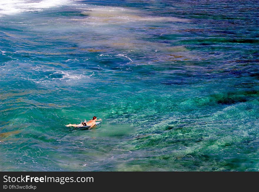 A surfer paddles out to catch some waves in a remote cove on Kauai, Hawaii. The myriad of colors in the water reflect the shallow coral reef that rises up out of the deeper blue water. Learn more about Pacific coral reefs at coralreefs.wr.usgs.gov/ Photographer: Susan Hazlett, USGS