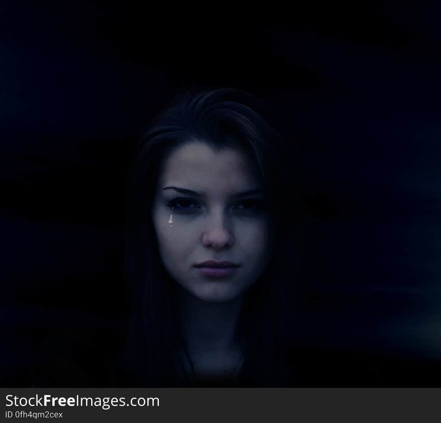 Portrait of crying young woman in shadows with tear rolling down face.