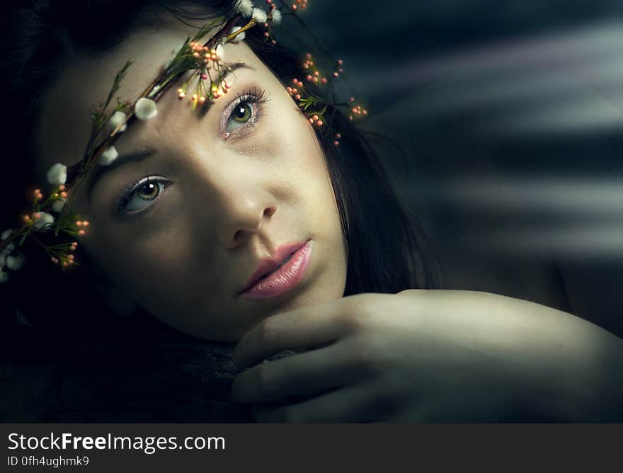 Portrait of beautiful young woman with band of flowers in hair, dark background with shafts of light. Portrait of beautiful young woman with band of flowers in hair, dark background with shafts of light.