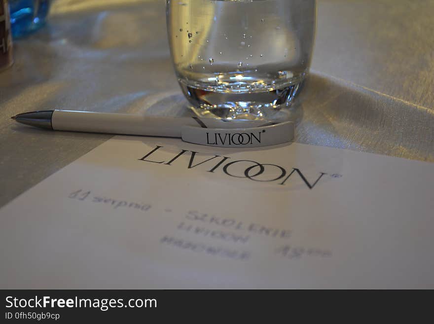 A close up of paper sheet and pen with company logo and a glass of water on a table. A close up of paper sheet and pen with company logo and a glass of water on a table.