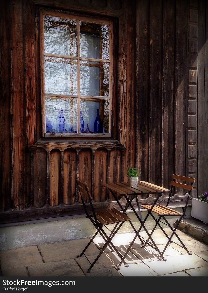 A pair of chairs and a table next to an old wooden house. A pair of chairs and a table next to an old wooden house.