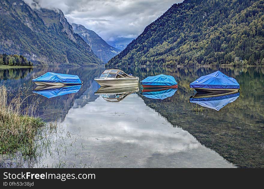 Covered boats reflecting on lake surface and coast mountains in the background. Covered boats reflecting on lake surface and coast mountains in the background.