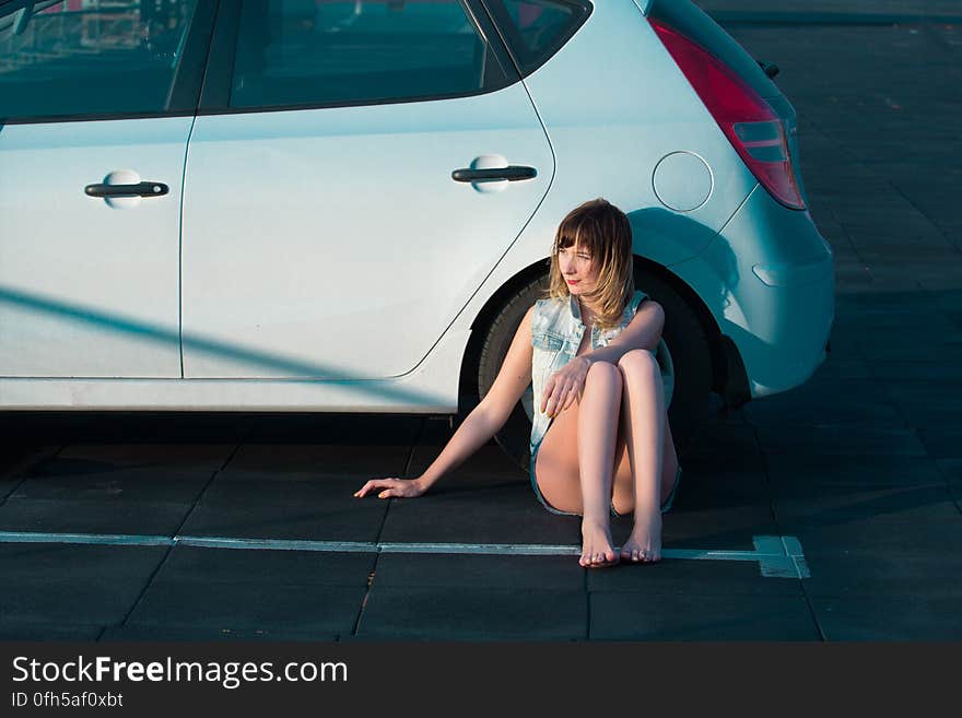 A young woman sitting on the ground beside a car. A young woman sitting on the ground beside a car.