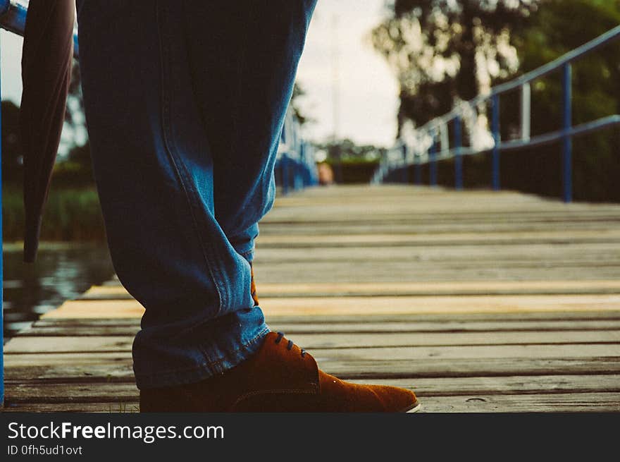 A person with blue jeans and brown shoes standing on wooden pier. A person with blue jeans and brown shoes standing on wooden pier.